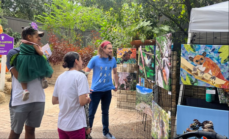 Eric Wuesthoff talking to two adults and a child next to photographs and collage artwork of lemurs outdoors.