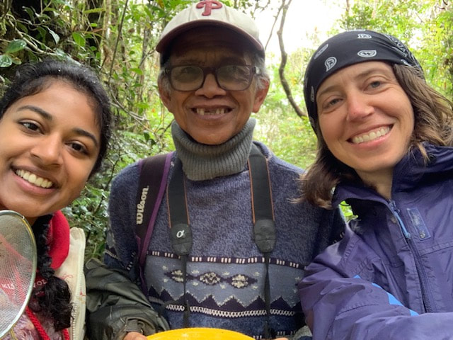 Three people with a sieve and colored plate smile for a selfie in a forest.