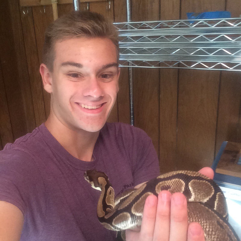 Photo of Eric Wuesthoff in a room smiling at the camera and holding a snake.