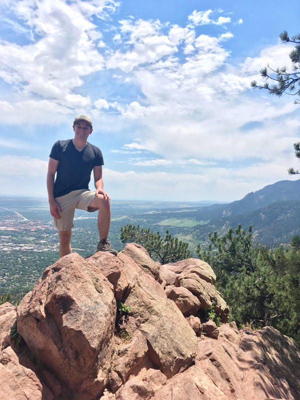 Photo of Eric Wuesthoff standing on top of a rock outcrop with mountains and a valley in the background.