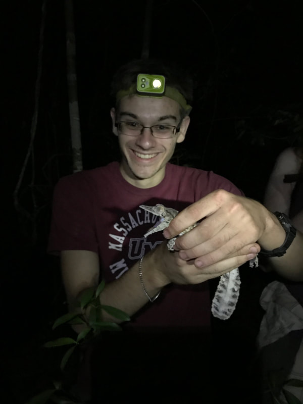 Photo of Eric Wuesthoff wearing a headlamp and holding a lizard with its mouth open.