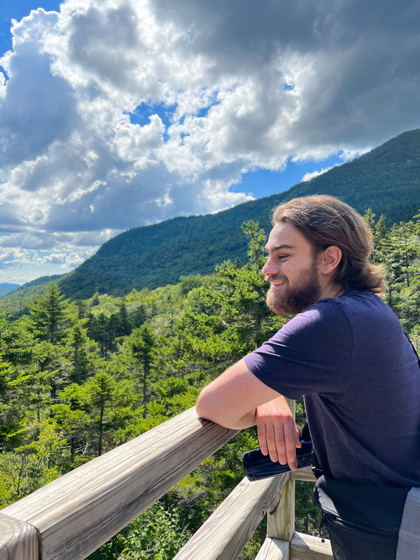 Photo of Eric Wuesthoff leaning on a railing overlooking pine forest.